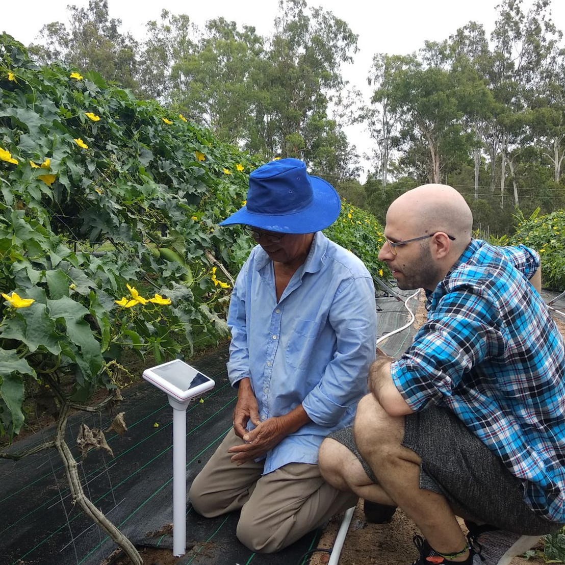 Two people beside a soil sensor in a planted field